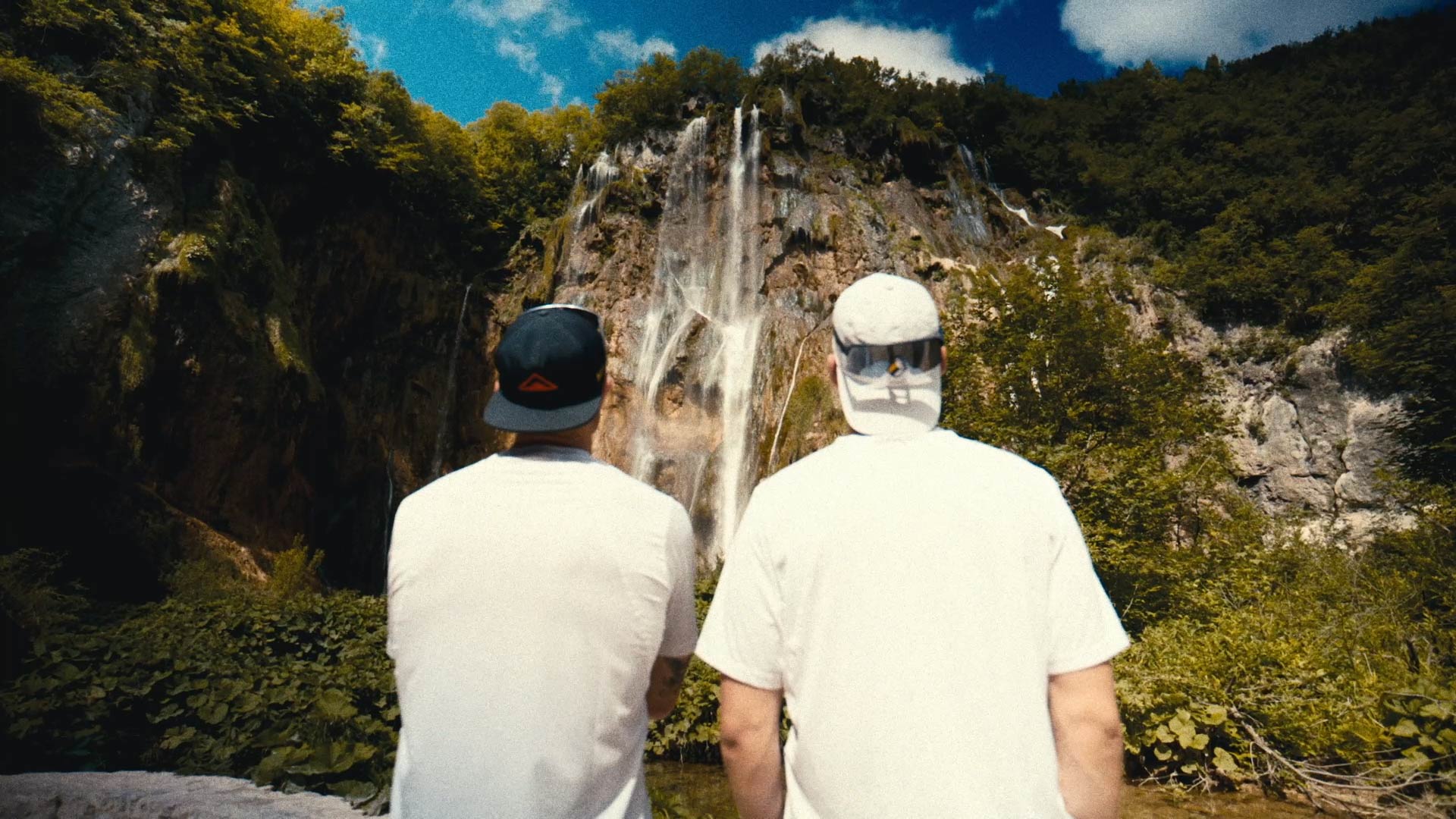 Cinematic 16:9 frame from the Red Bull marathon documentary: two runners facing the Plitvice waterfalls